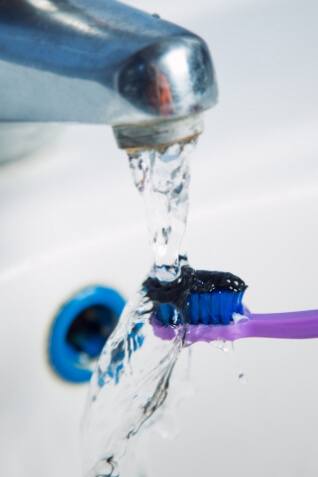 Toothbrush with black toothpaste being rinsed in a sink