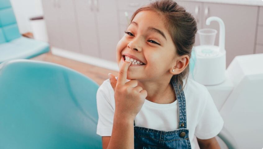 Young girl in dental chair pointing to her smile