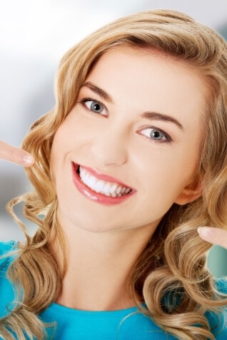 Woman with curly blonde hair pointing to her smile