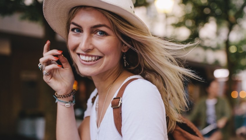 Smiling young woman in sunhat outdoors after receiving dental services in Yarmouth