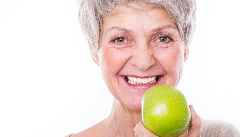 Woman with gray hair holding apple and smiling