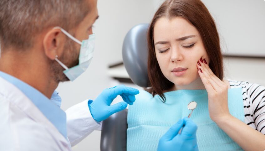 Woman wincing and touching her cheek while visiting emergency dentist in Yarmouth