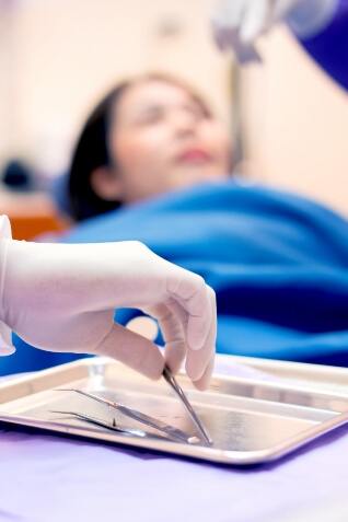 Dentist picking up dental instrument on tray while treating a patient