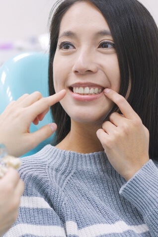 Woman in dental chair pointing to her smile