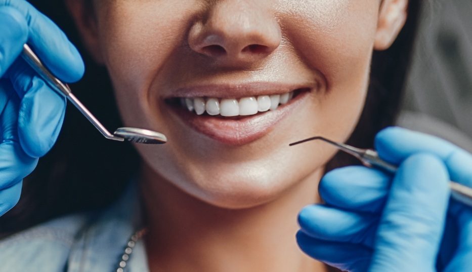 Close up of dentist holding dental instruments in front of a patient's smile
